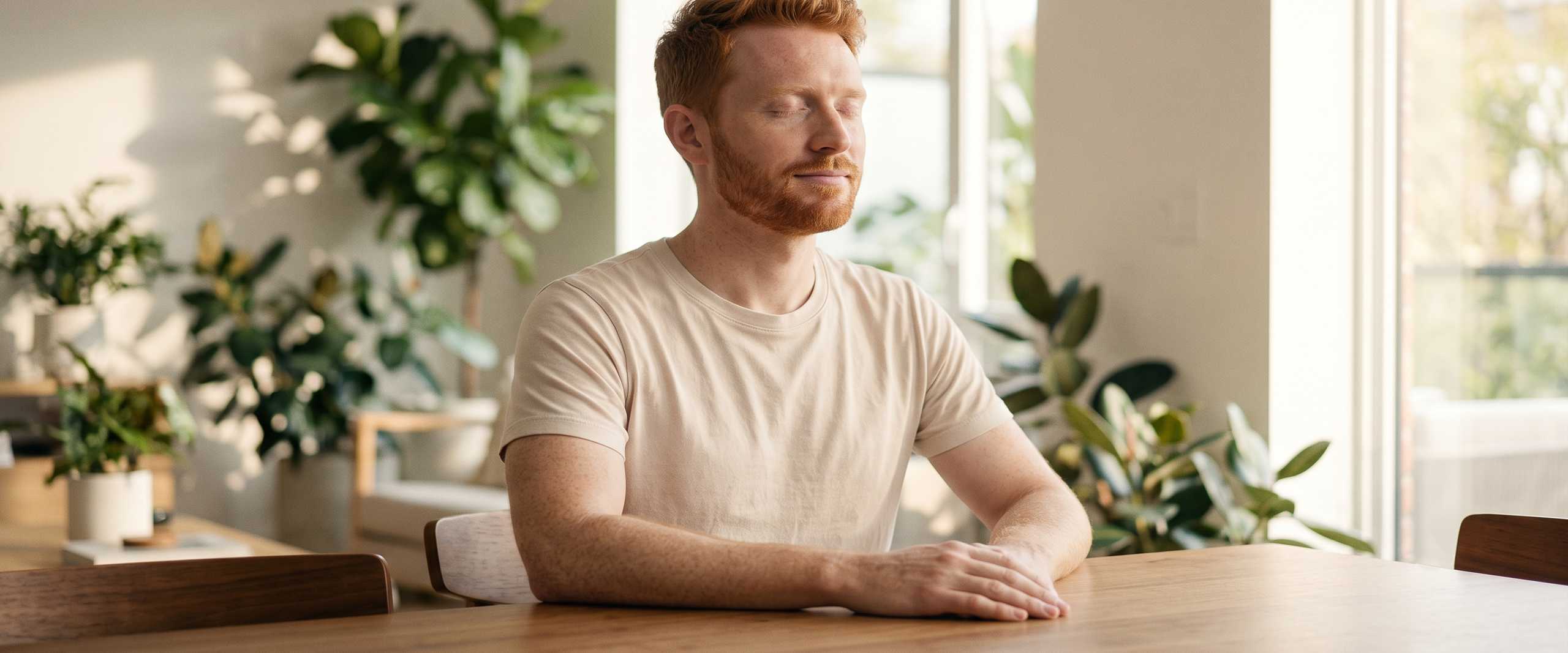An adult with eyes closed and a soft half-smile of recall, phone resting face-down on a wooden table beside them, the quiet moment of testing yourself and finding you remember